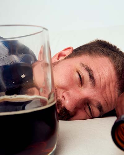 мужчина лежит на кровати рядом с кружкой пива